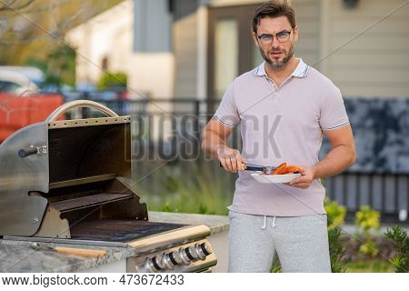 Man Cooking Meat On Barbecue In The Backyard Of The House. Handsome Man Preparing Barbecue Salmon Fi