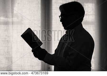 Profile View Of A Mature Man Focused On Reading A Book, Male Silhouette Standing In Front Of A Windo