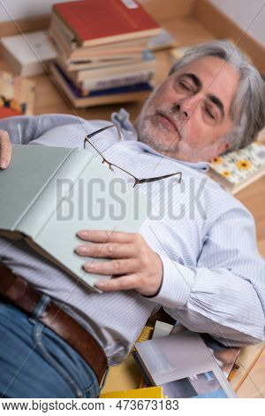Mature Man With Grizzled Beard And Hair Sleeping Among Many Books Distributed On The Floor. Falling 