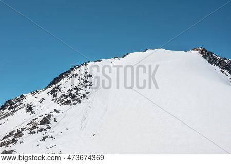 Climbers Footprints On Steep Snowy Slope Of High Snow Mountain With Rocks On Top. Snow-white Mountai