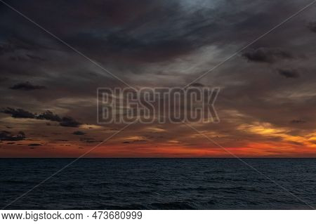 View Of The Sea At Dusk Against An Overcast Sky.\nclouds Catch The Last Red-orange Rays Of The Setti