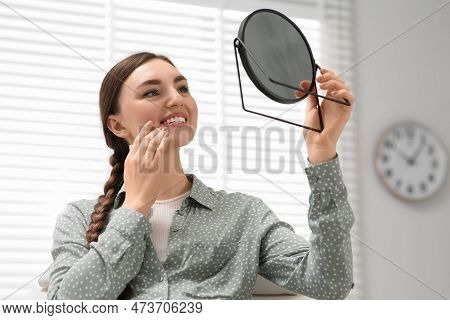 Young Woman Looking At Her New Dental Implants In Mirror Indoors
