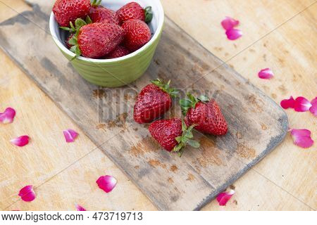 Above View Of Wet Wooden Board With Bowl With Strawberries And Three Strawberries Lying On Table. Co