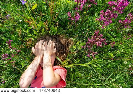 Portrait Of A Child Girl In Summer Lying In The Grass And Wildflowers With Heels And Palms. Summer T