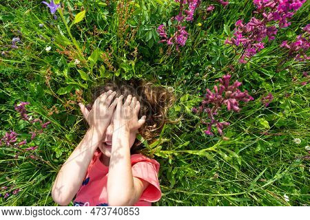 Portrait Of A Child Girl In Summer Lying In The Grass And Wildflowers With Heels And Palms. Summer T