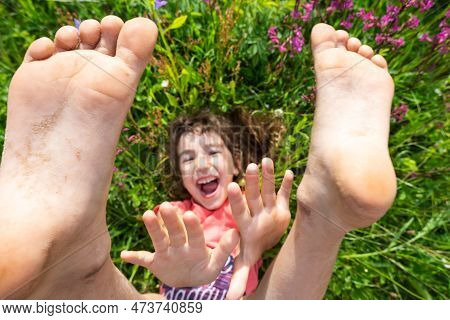 Portrait Of A Child Girl In Summer Lying In The Grass And Wildflowers With Heels And Palms. Summer T