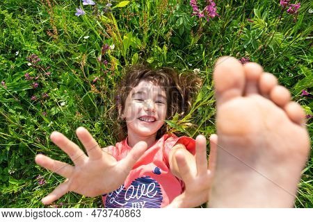 Portrait Of A Child Girl In Summer Lying In The Grass And Wildflowers With Heels And Palms. Summer T
