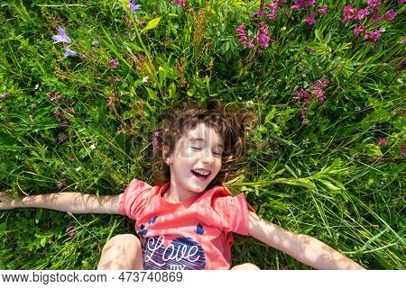Portrait Of A Child Girl In Summer Lying In The Grass And Wildflowers With Heels And Palms. Summer T