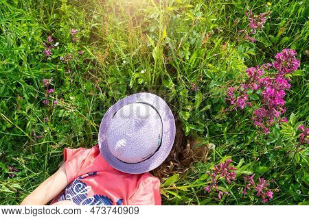 Portrait Of A Child In A Hat With His Face Covered In Summer Lying In The Grass And Wildflowers. Hat