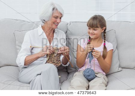 Nieta aprendiendo a tejer con la abuela sentada en el sofá