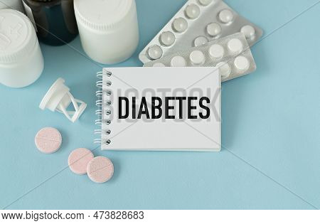 Diabetes Text On White Paper In Notebook Near Pils On Blue Background.