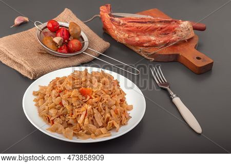 Stewed Cabbage - Bigos In A White Porcelain Plate Against The Background Of A Piece Of Smoked Meat A