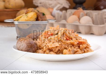 Braised Cabbage - Bigos And Grilled Sausage In A White Porcelain Plate Against The Background Of Chi