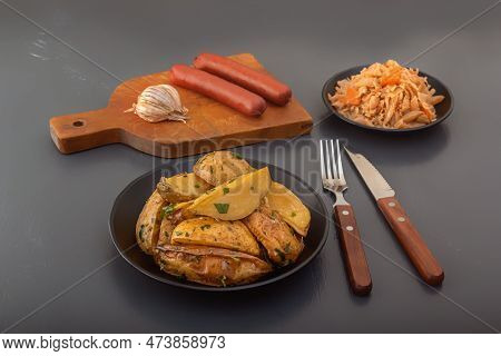 Baked Potato Wedges With Herbs And Salt In A Black Plate With Smoked Sausages And Stewed Cabbage On 