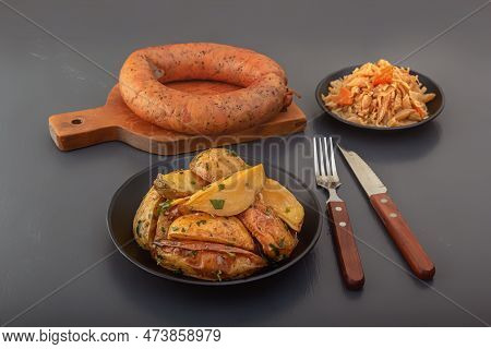 Baked Potato Wedges With Herbs And Salt In A Black Plate With A Circle Of Smoked Sausage And Stewed 