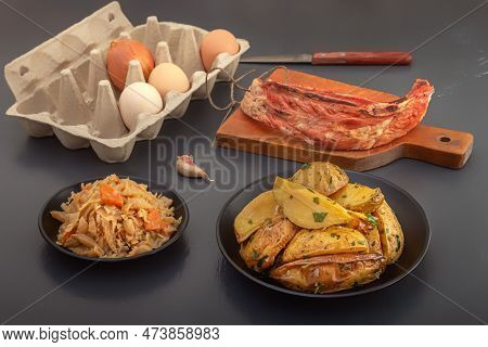 Baked Potato Wedges With Herbs And Salt In A Black Plate With A Piece Of Smoked Meat And Stewed Cabb