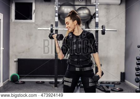 Electrical Muscle Stimulation, Ems Training Studio. A Sporty Girl Wearing An Ems Suit Doing Dumbbell