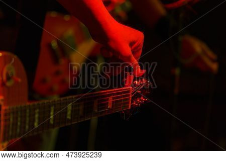 The Guitarist Tunes The Guitar Holding On To The Peg In The Spotlight. Guitar Tuning