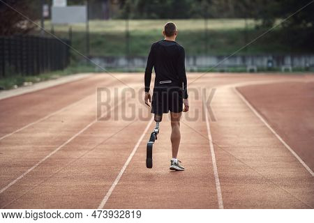 Rear View Of A Runner With Artificial Leg Walking On Running Track At The Stadium.