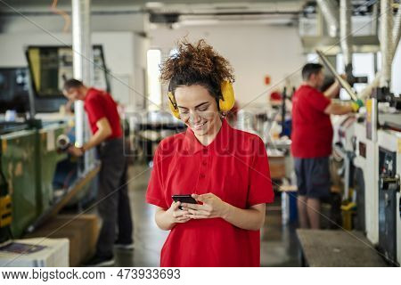A Female Inspector With Antiphons Looking At The Phone In Printing Shop.