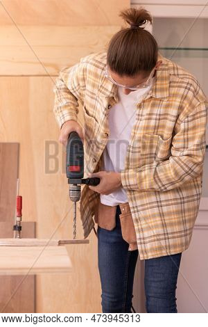 Focused Male Carpenter Drilling Hole In Wood Plank With Electric Drill While Working In Home Carpent
