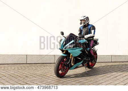 Guy Motorcyclist In Professional Protective Equipment And Helmet Sits On Sports Motorcycle Against W