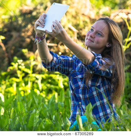 Nice teengirl in nature and taking selfie on a tablet PC 