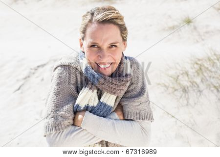 Attractive shivering blonde standing on the beach on a bright but cool day