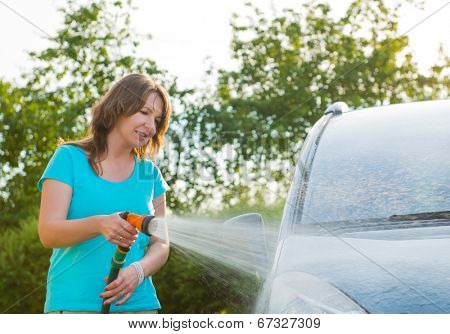 Woman washing her car in garden without detergents in ecological way.
