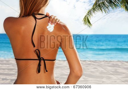 Woman applying sun protection on tanned back