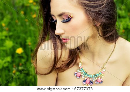 beautiful young girl with long hair and beautiful makeup with necklace on the neck sitting on the gr