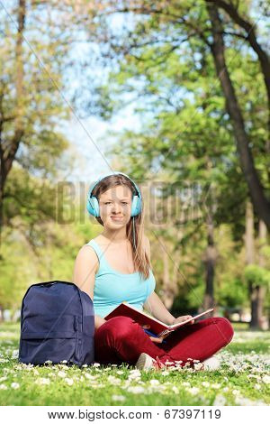Young girl with headphones studying in park seated on grass