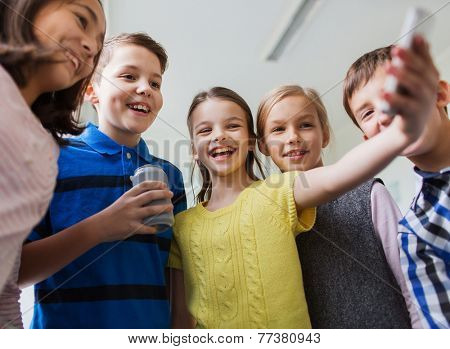 education, elementary school, drinks, children and people concept - group of school kids with smartphone and soda can taking selfie in corridor