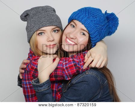 Fashion portrait of two stylish sexy hipster girls best friends, wearing cute swag outfits and hats. Over gray backround.