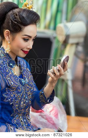 BANGKOK, THAILAND, February 17, 2015: A Thai lady dancer is checking her makeup make up on a mirror before the show at the Krung Kasem floating market in the Thewet district of Bangkok, Thailand