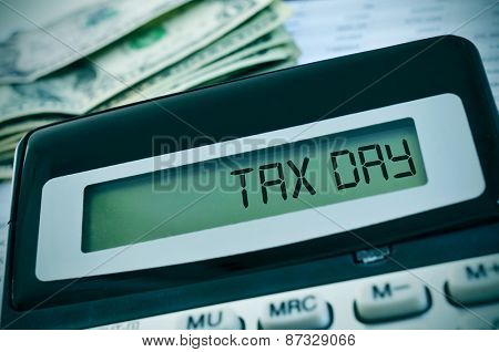 closeup of the the display of a calculator with the text tax day written in it and a pile of dollar banknotes in the background