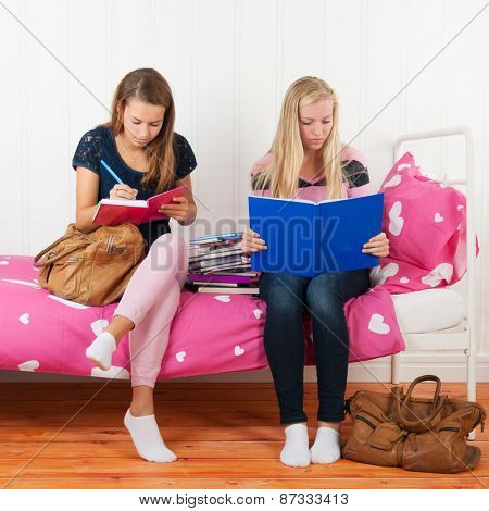 two teengirls sitting on bed making homework together