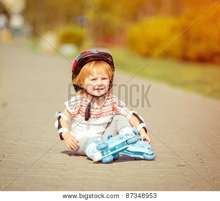 two year old pretty girl in roller skates and a helmet sitting on the street