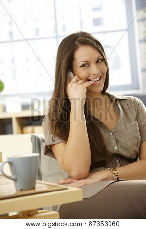Young woman talking on mobilephone with an impish smile biting her little finger.
