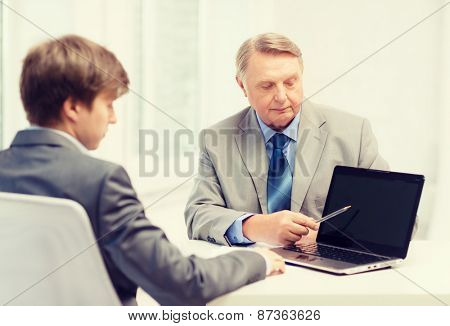 business, advertisement, technology and office concept - older man and young man with laptop computer in office