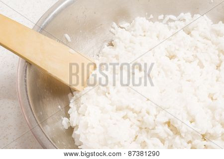 Cooked white rice in a metal bowl and wooden spoon stirrer