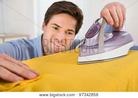 Young Man Ironing T-shirt With Electric Iron