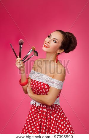 Smiling Woman with makeup brushes. She is standing against a pink background.