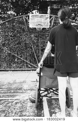 Woman Holding Wheel Chair  With With Sitting Man At Basketball Court