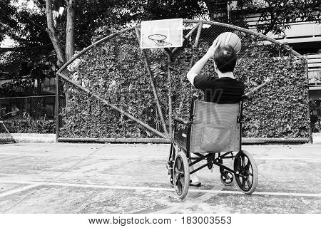 Man Sitting On Wheel Chair With Broken Leg In Plaster Cast , Try To Shoot Basketball  At Court