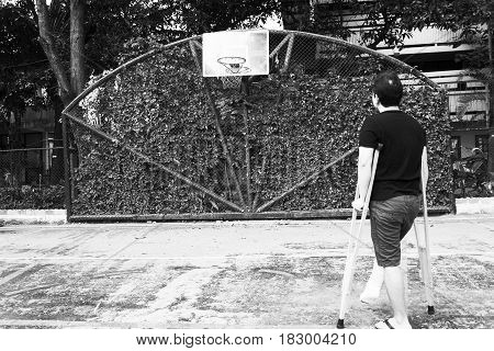 man standing with broken leg in Plaster cast using Crutches at basketball court in white tone