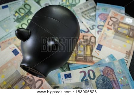 Selective focus on Black piggy bank on pile of Euro banknotes as saving concept.