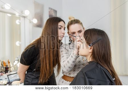 makeup teacher with her student girl. Makeup tutorial lesson at beauty school. Visagiste applying makeup on the eyes. Makeup master class