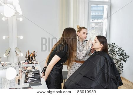makeup tutorial lesson at beauty school. Makeup teacher training her student girl to become makeup artist. Real people. Portrait of visagiste applying makeup on the eyes. Makeup master class