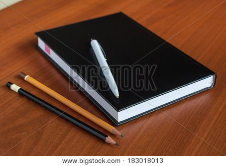 Black Diary, Or Sketchbook With Pen And Pencil On Th Table
